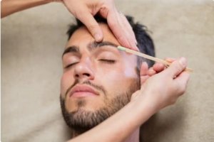 A cose up of a mans face while he is having his eyebrows waxed.